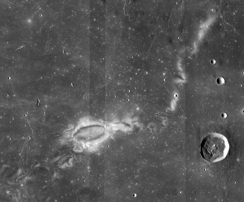 Swirls on the moon: Flat, dark gray terrain seen from above. Bright tendril-like swirl snakes across the surface.