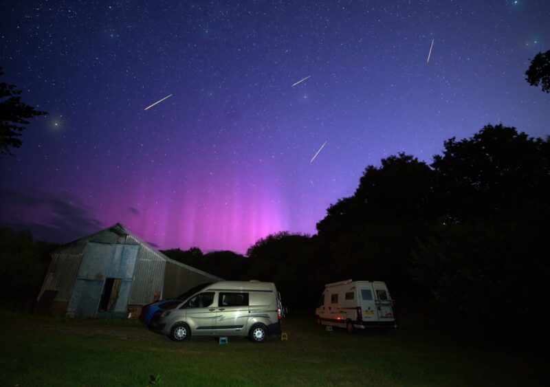 Purple and pink sky with 4 streaks and a couple of vehicles in the foreground.