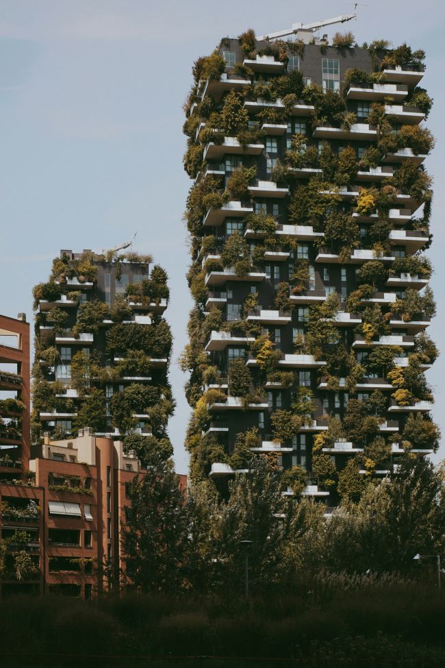 Two tall buildings covered in trees and plants.