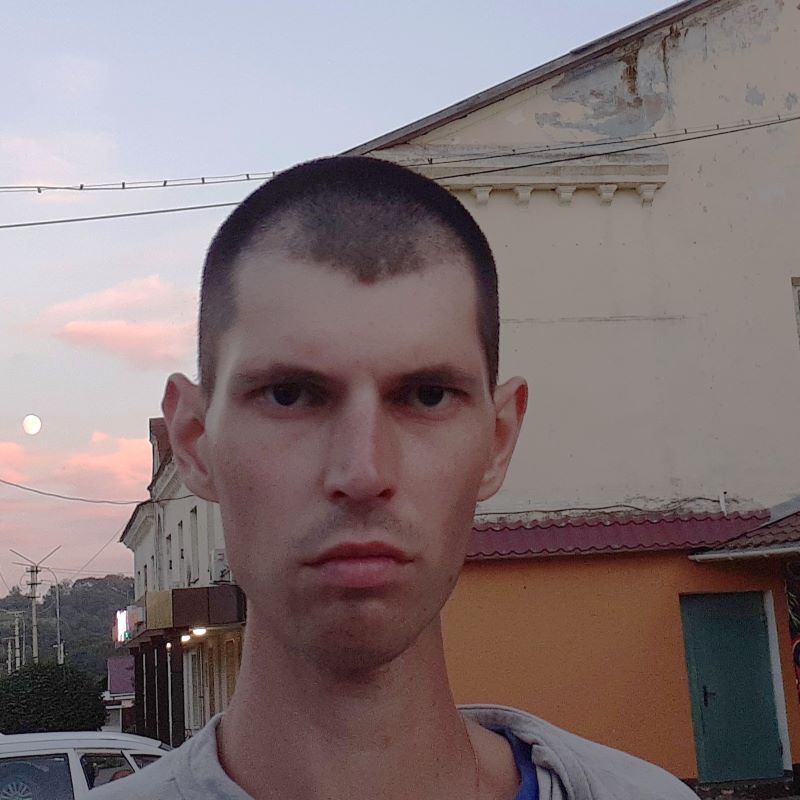 A man with close-cut hair looking into the camera with the moon over his shoulder.