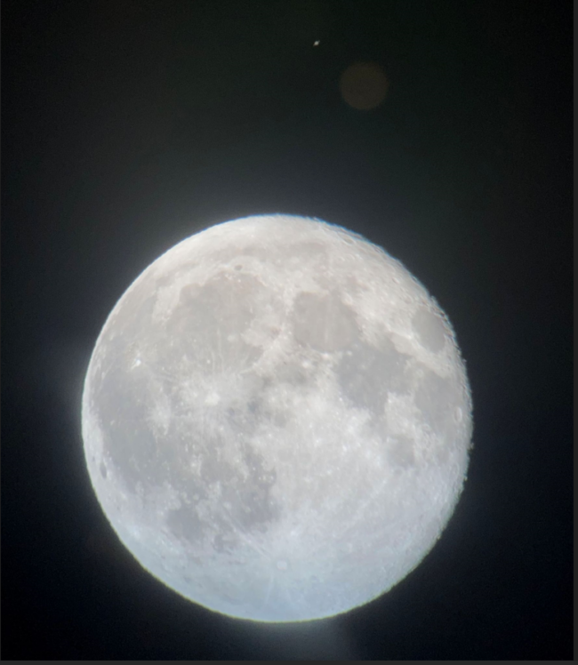 Bright white sphere with some darker areas in the middle. There is a small dot above the sphere.