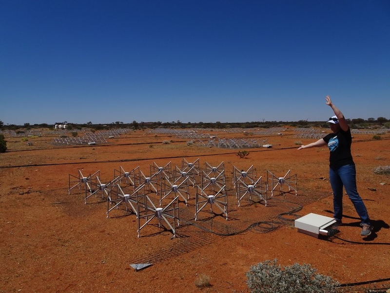 SETI: Array of 16 small X-shaped metal structures on barren terrain. A woman is standing next to them with her arms raised.