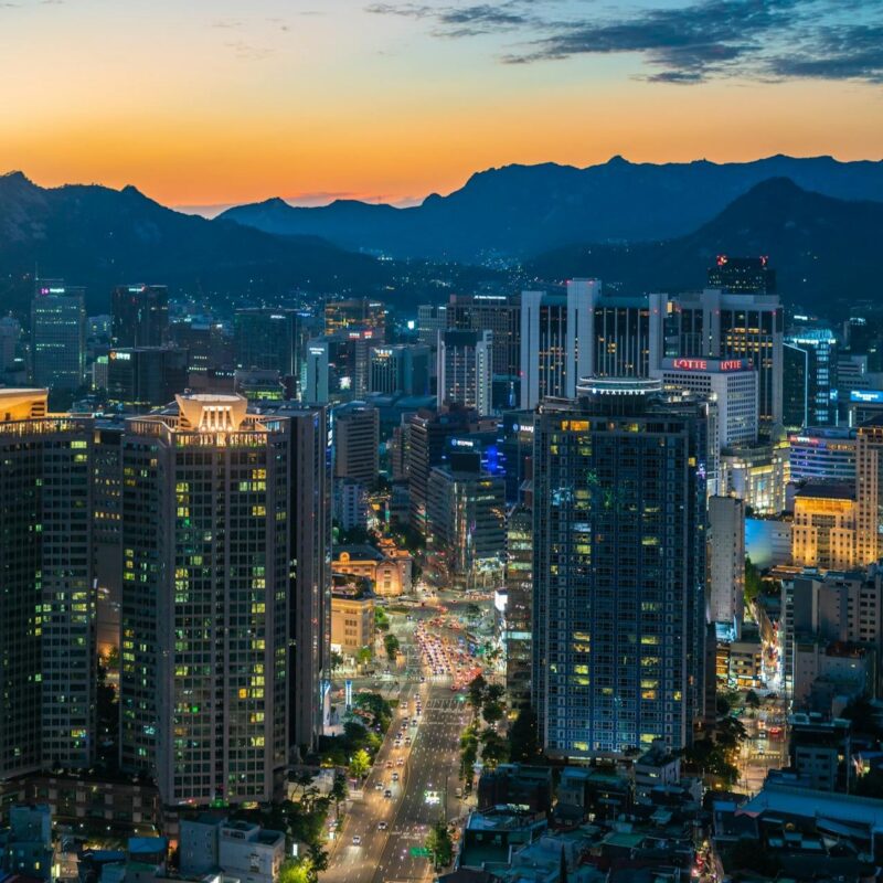 Cities: Looking down at tall buildings lit at dusk with mountains behind.