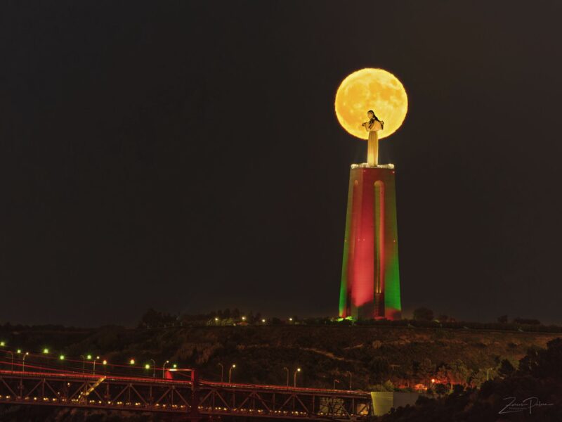 Big building with a statue of Jesus Christ at the top. A yellowish, bright moon behind the statue.