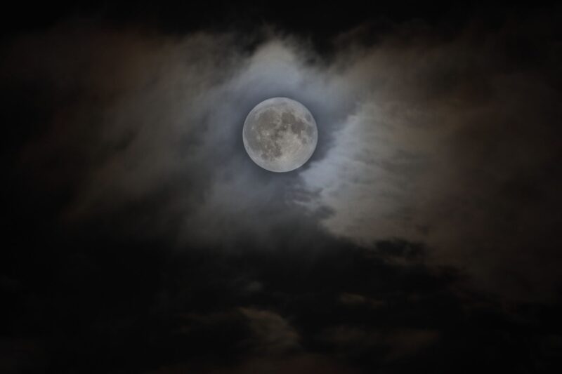 Gray sphere surrounded by clouds. The moon is so bright that it illuminates big part of the dark sky.