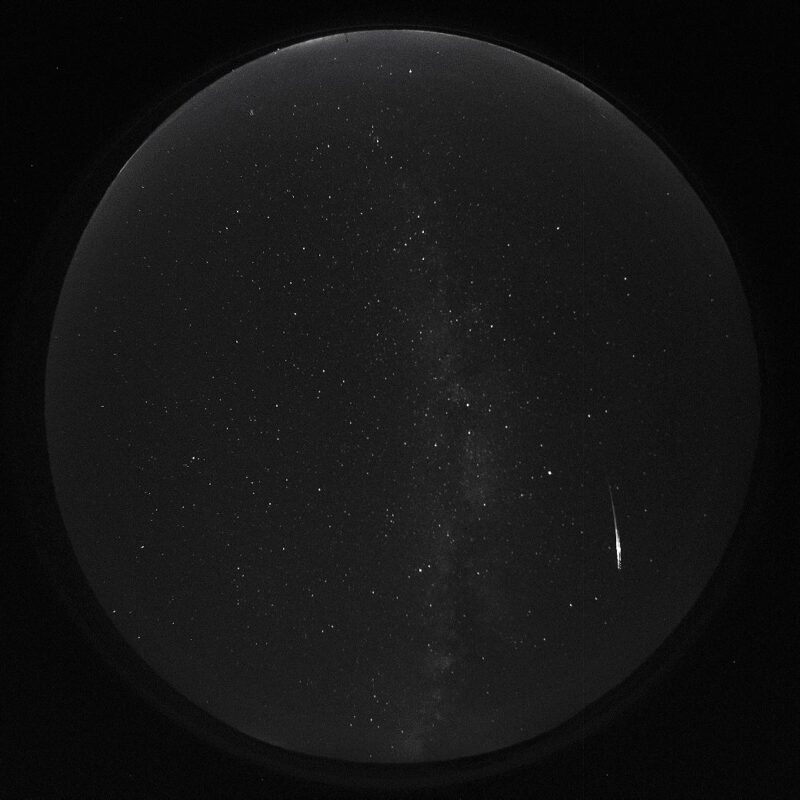 Circle with a dark sky, many dots, and a bright streak on the bottom right,