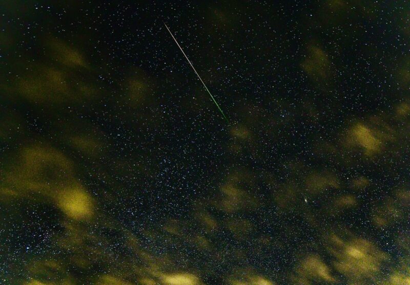 Dark sky with many stars and yellow clouds. There is a bright streak at the top.