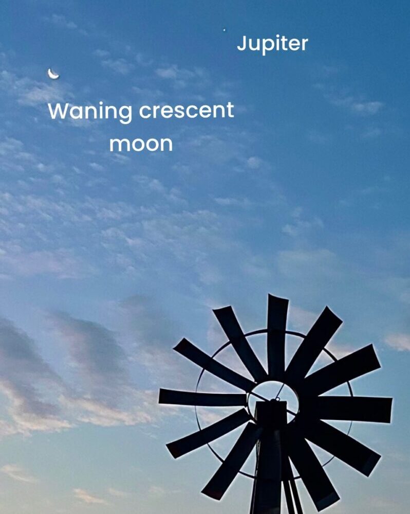 Top of a windmill and some clouds on daylight. The moon on the left, a little dot for Jupiter to the right.