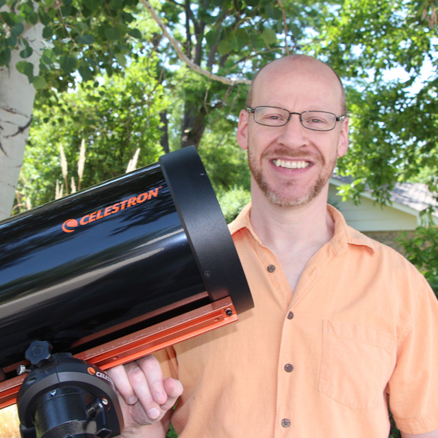 What's Phil thinking: Smiling man in glasses and light-colored shirt, standing next to a telescope.