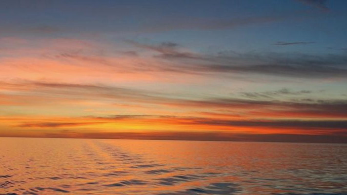 Super-Marine Heatwave: Bands of clear sky and clouds at sunset over rippling water in wide panorama.