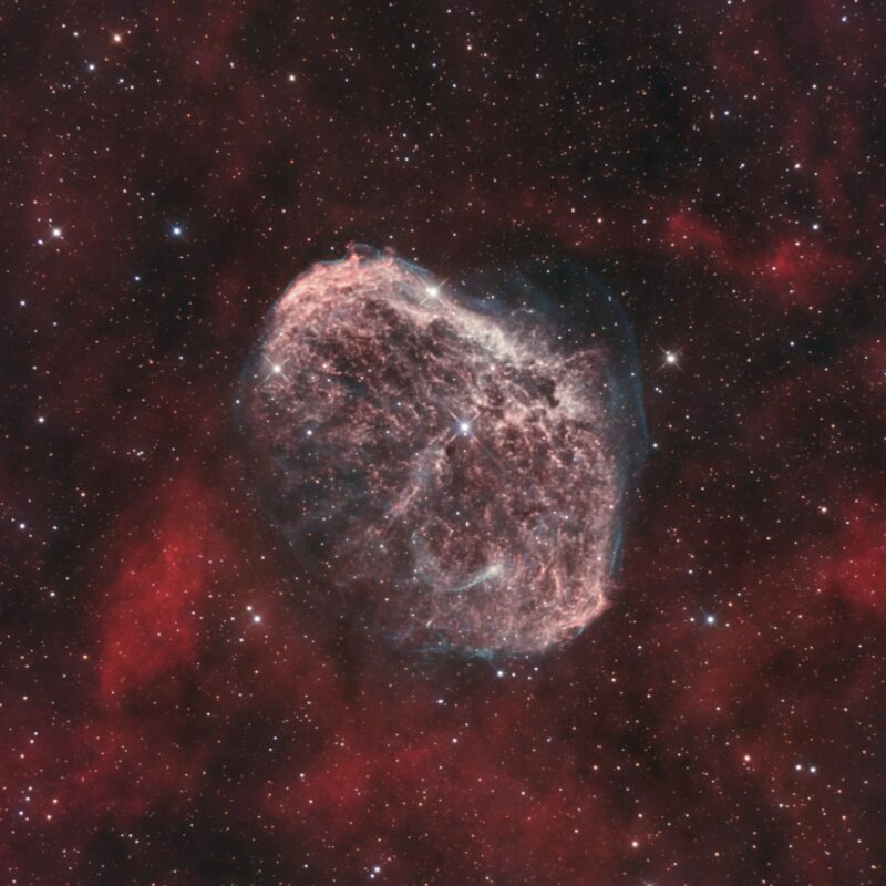 A large, pink cocoon of gas overlaid with prolific red clouds and numerous stars.