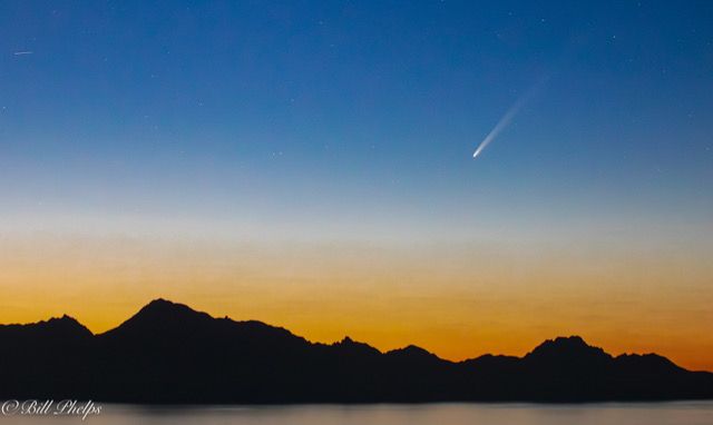 Blue and orange sky with white comet and mountains.