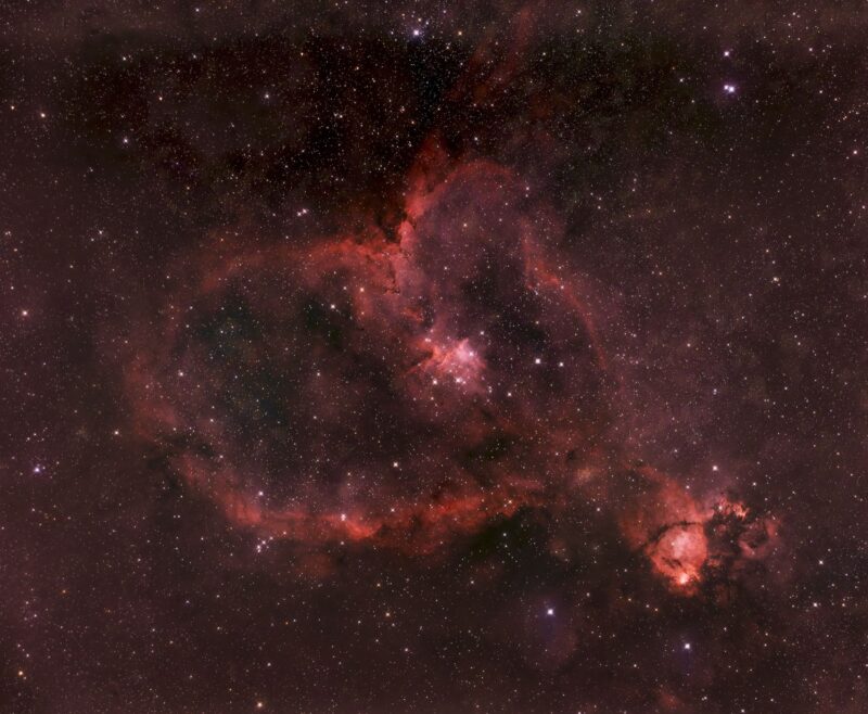 A bright, large and reddish heart-shaped nebulosity over a multitude of distant stars.