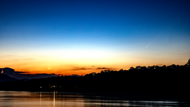 Orange, white and blue sky with moon at left and comet at right.