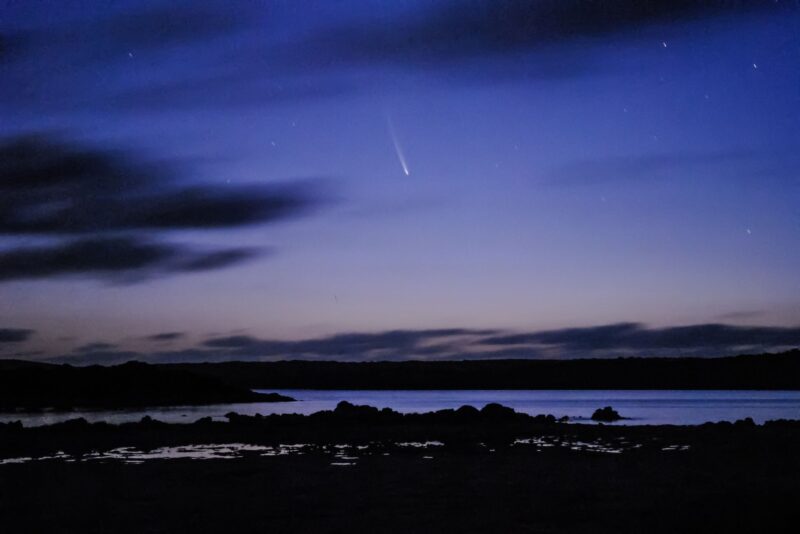 Some clouds and a brightening blue sky with a comet at center.