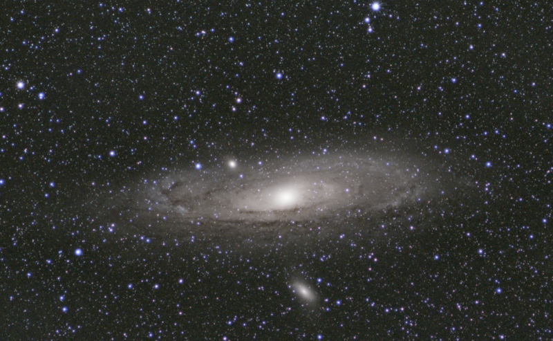 Large whitish nebula with a bright nucleus, dark lanes and thousands of foreground stars.