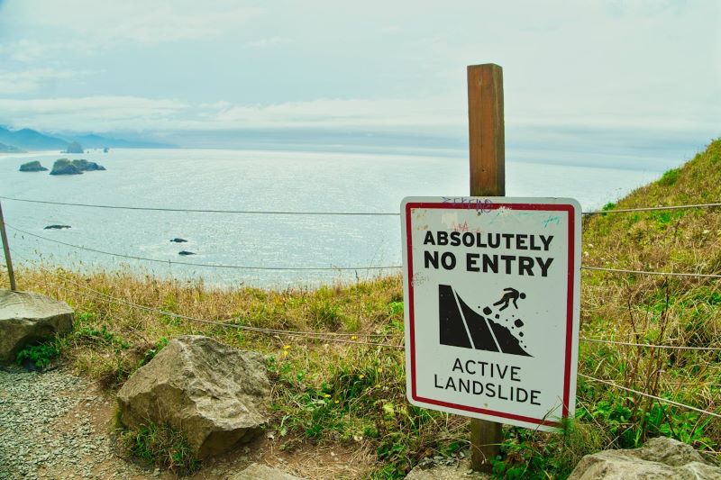 Landslide warning sign on a barbed wire fence on the coast of a large body of water.