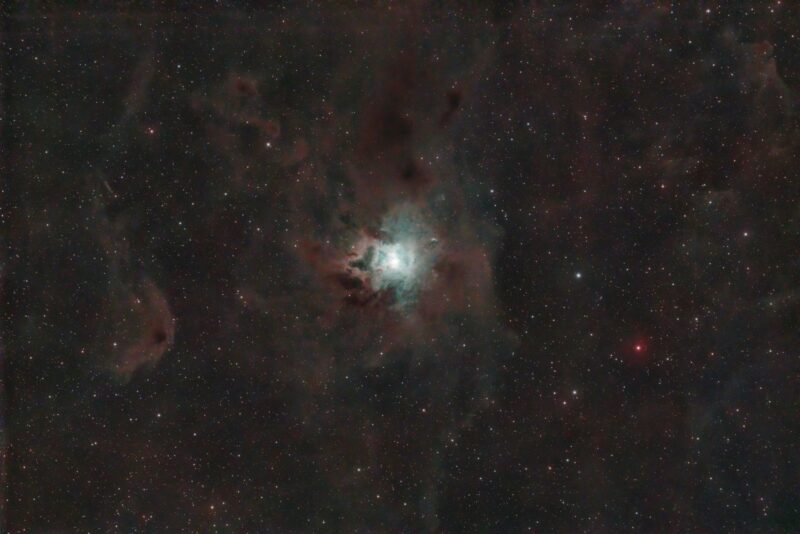 Small, bright whitish nebula embedded in swirls of darker clouds in a star field.