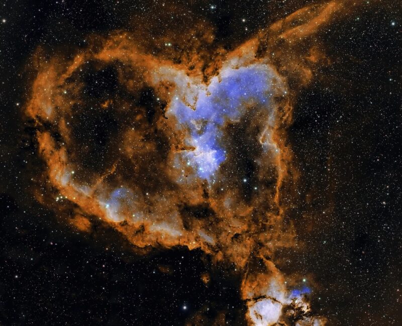 A large, bright, mostly orange heart-shaped nebulosity in a field of distant stars.