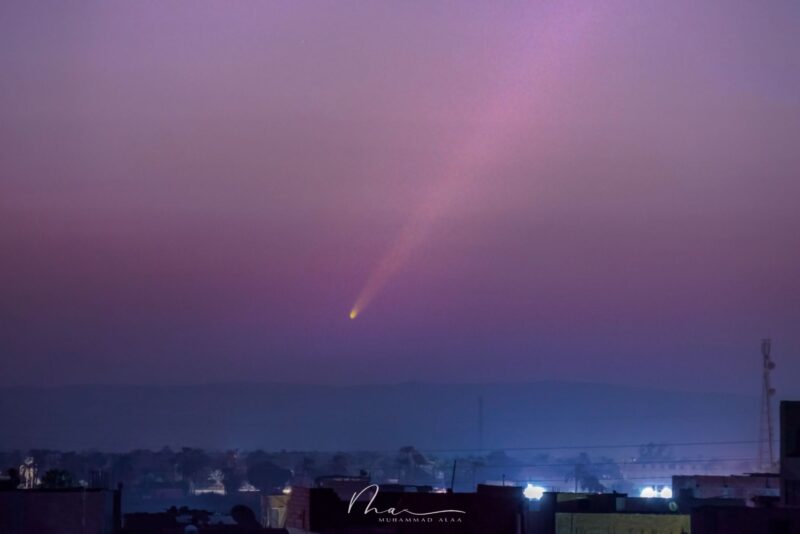 Purplish skies with a comet and a long tail over a dark village.