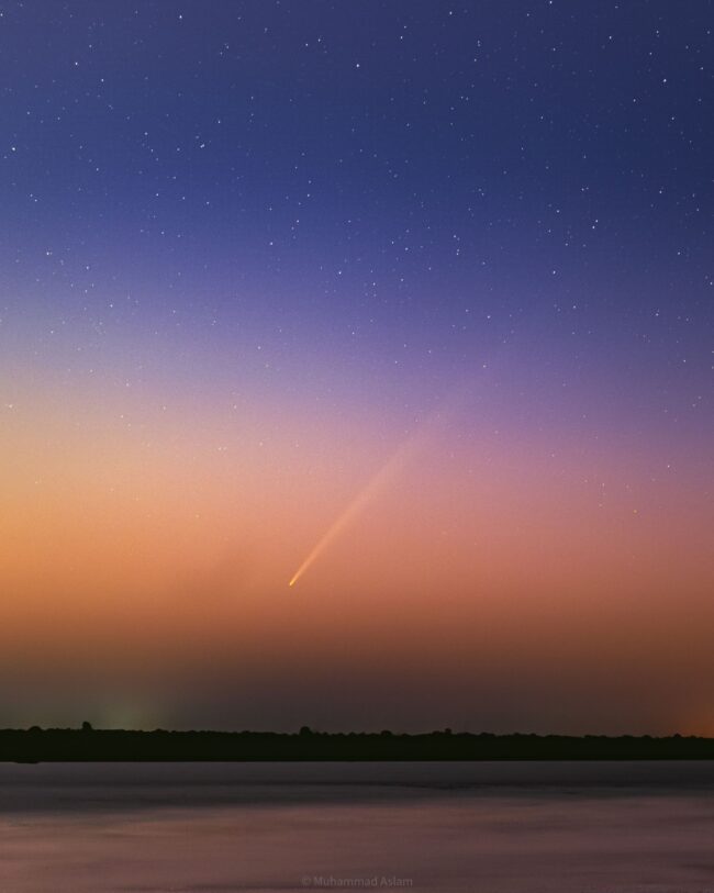 Twilight sky with a comet with long tail cutting across from lower left to upper right.