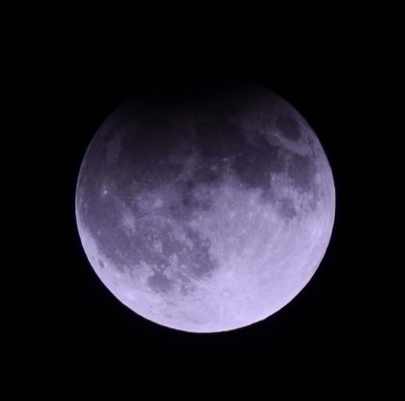 A bluish full moon with a darkening on the top.