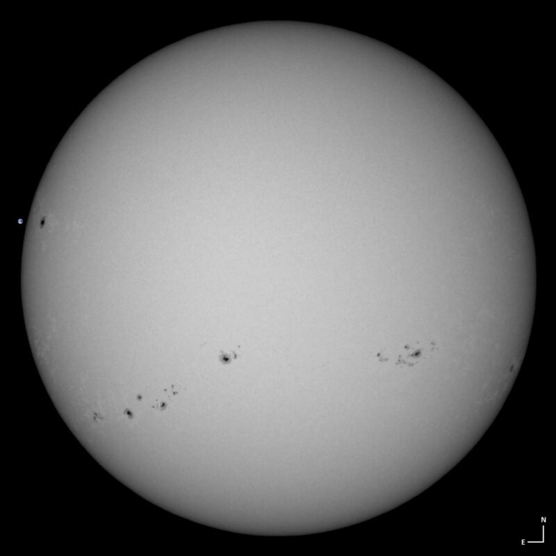 The sun, seen as a large white sphere with small dark spots.