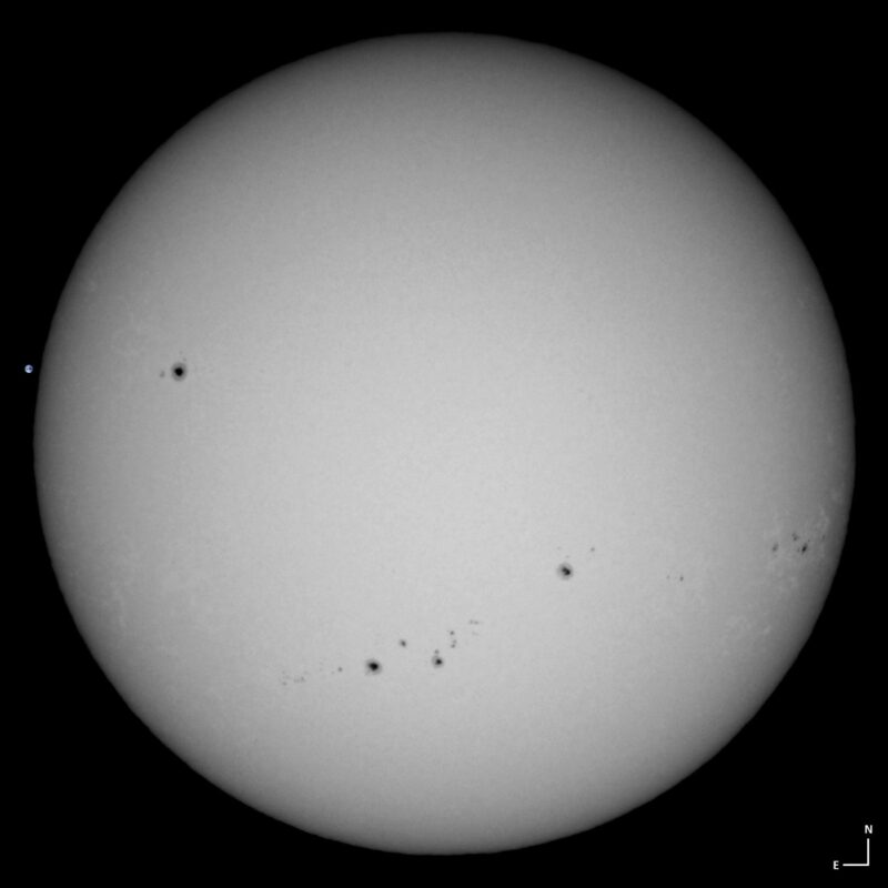 The sun, seen as a large white sphere with small dark spots.