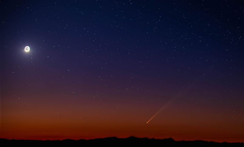 Moon at upper left with the comet and a colorful sky,