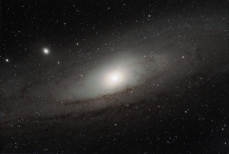 Large whitish nebula with a bright nucleus, dark lanes and thousands of foreground stars.