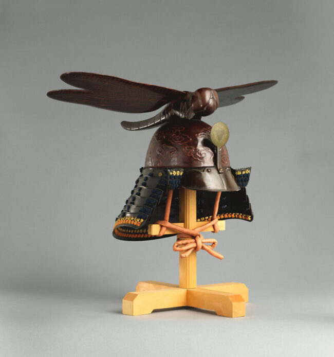 Brown metal Japanese helmet. It has a big dragonfly, with a wingspread much wider than the helmet, mounted on top.