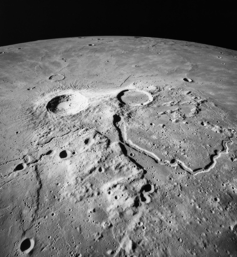 Oblique view of gray cratered terrain on planet-like body. A long valley snakes across the middle right of the image.