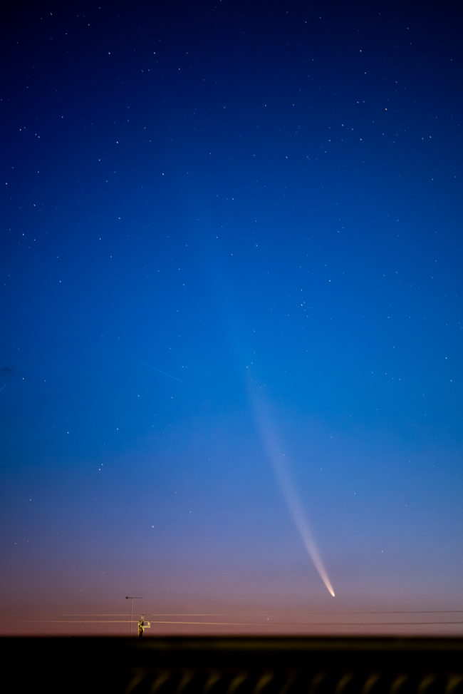 Vertical blue sky with pink at the horizon and a white comet with long tail.