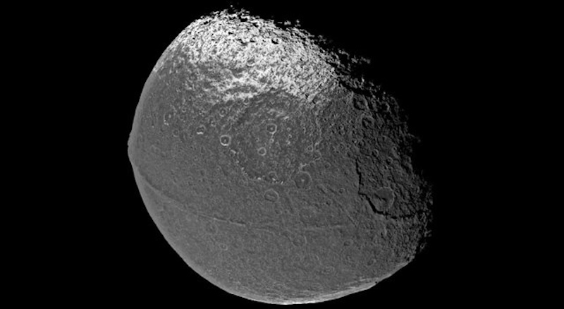 Gray rocky planet-like sphere with white patch at the top and tall thin ridge going around its middle.