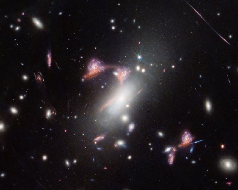 Many small oblong galaxies on black space. In the center, pink streaks of light form a question mark.