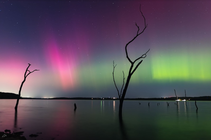 Aurora is the distance behind a lake a tree.