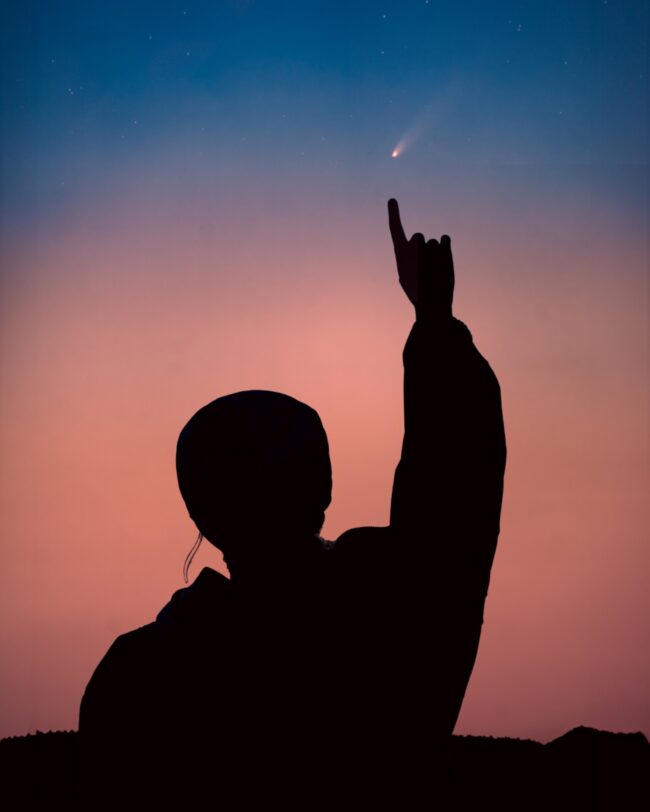 Silhouette of a person pointing up at a comet.