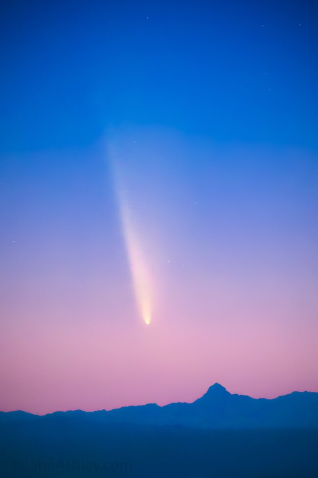 Pink and blue sky with mountain range and a bright comet.