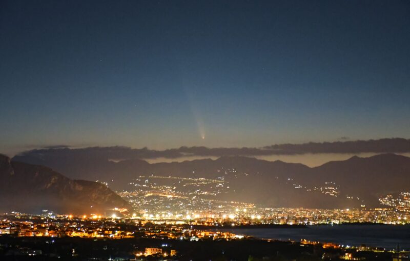 City lights with a comet in the sunset sky above.