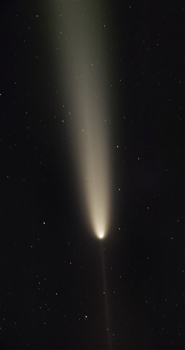 Bright comet in dark sky with a thin light extending from the head downward.