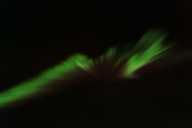 A green aurora seen from below as a wiggly diagonal line across the sky.