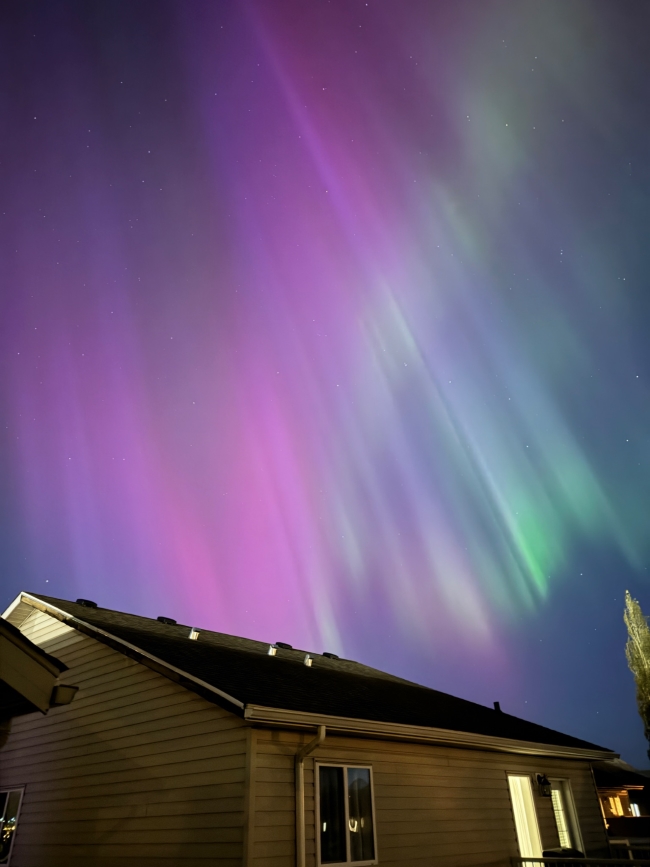 Purple and green aurora in distinct diagonal lines over the roof of a house.