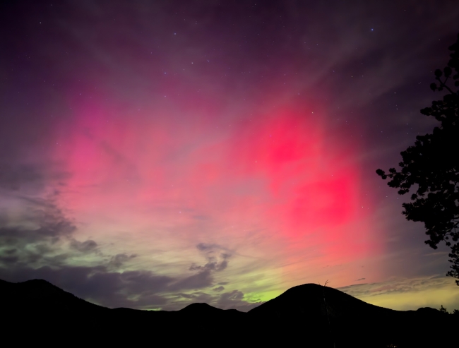 A bright magenta auroral display over silhouetted mountains.