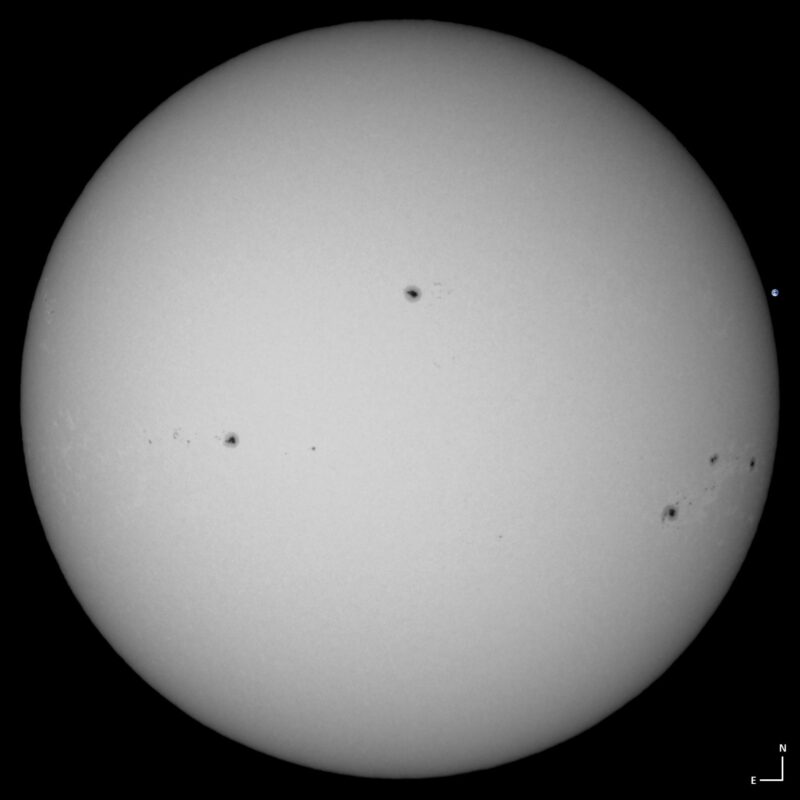 The sun, seen as a large white sphere with small dark spots.