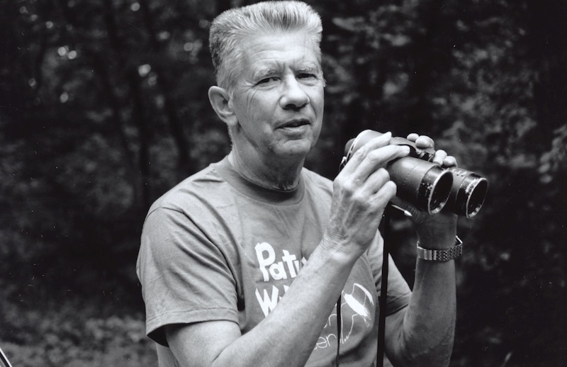 A black and white image of an older man holding a pair of binoculars.