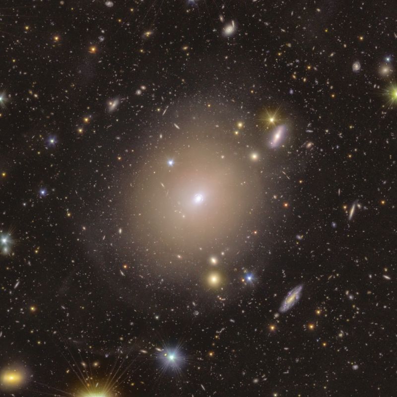 View into space with many small galaxies and one larger fuzzy one with a ring tight around its center showing 4 bumps.