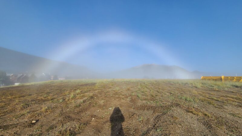 A white rainbow with a person's shadow in the foreground.