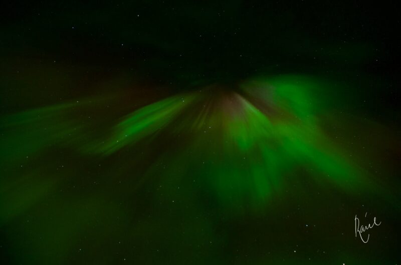 Bright green streaks of light high above in a black sky.