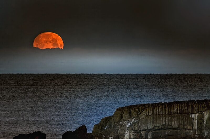 Half top of the moon. It looks orange. Dense fog covers the bottom half.
