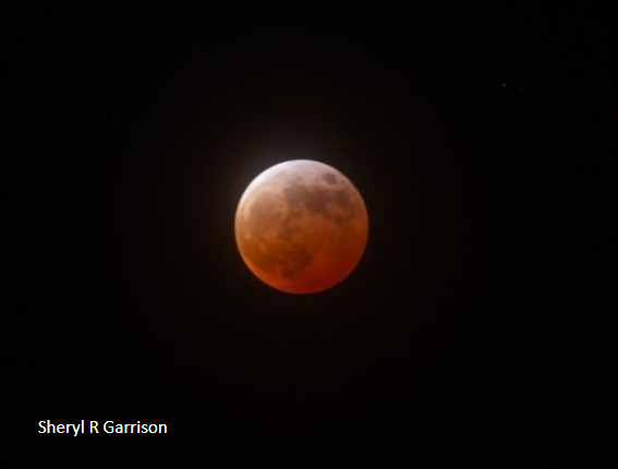 A full moon that looks reddish at the bottom right, orange at the bottom left, and white at the top.